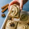 Close-up of chai cinnamon rolls with glossy brown-sugar caramel bottoms and chai cream-cheese frosting, arranged in a rustic baking dish.
