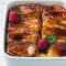 Golden crème brûlée French toast casserole with caramelized top, fresh berries, and powdered sugar on a white serving plate.