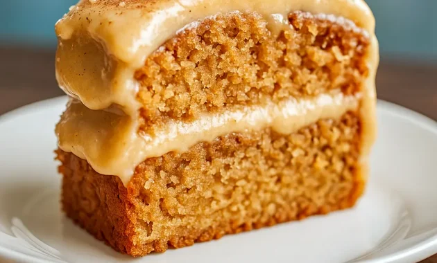 Slice of applesauce spice cake topped with cinnamon cream cheese frosting and chopped pecans on a ceramic plate.