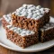 Bowl of chocolate-coated Rice Krispie Cereal coated in powdered sugar, looking like crunchy Rice Crispy Treats meets Classic Muddy Buddies, perfect for no-bake snacking.