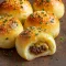 Golden-brown garlic Parmesan cheeseburger bombs on a platter, each one oozing melted cheddar with a sprinkle of grated Parmesan and chopped parsley, served with a bowl of dipping sauce.