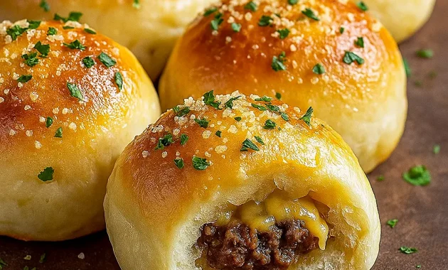 Golden-brown garlic Parmesan cheeseburger bombs on a platter, each one oozing melted cheddar with a sprinkle of grated Parmesan and chopped parsley, served with a bowl of dipping sauce.