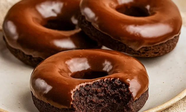 Close-up of three glazed chocolate protein donuts on parchment with almond crumbs — a perfect visual for Healthy Sweet Protein Snacks, and a tempting idea for a Protein Air Fryer Dessert. This shot also reads as Gluten Free Paleo Desserts and Healthy Non Dairy Desserts, with a decadent Health Chocolate Desserts vibe; great for Dairy Free Healthy Meals, Healthy Gluten Free Baking Recipes, labeled as Macros Desserts and useful inspiration for Protein Powder Meals.