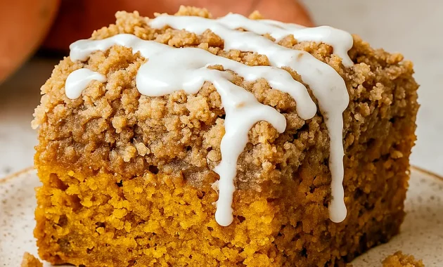 Overhead slice of pumpkin coffee cake with thick streusel topping and drizzle of glaze on a white plate.