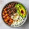 Overhead shot of a bowl with seasoned ground beef, roasted sweet potato cubes, sliced avocado, dollops of cottage cheese, and a honey drizzle, garnished with cilantro, Viral Hot Honey Ground Beef Bowl.