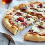 Thin-crust pizza topped with fig preserves, melted mozzarella, torn prosciutto and crumbled goat cheese, sliced on a wooden board.