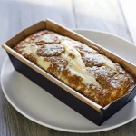 Slice of cinnamon swirl protein cake with visible cinnamon ribbon and moist crumb, plated with a fork and a sprinkle of cinnamon.
