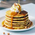 Stack of golden butterscotch-chip pancakes drizzled with butterscotch syrup and topped with whipped cream, styled for a festive Harry Potter–themed brunch.