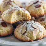 Stack of soft almond-ricotta cookies dusted with powdered sugar on a white plate, showing tender centers and sliced almond topping.