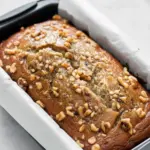 Sliced maple banana bread on a wooden board, showing moist crumb, toasted walnut pieces, and a glossy maple glaze.