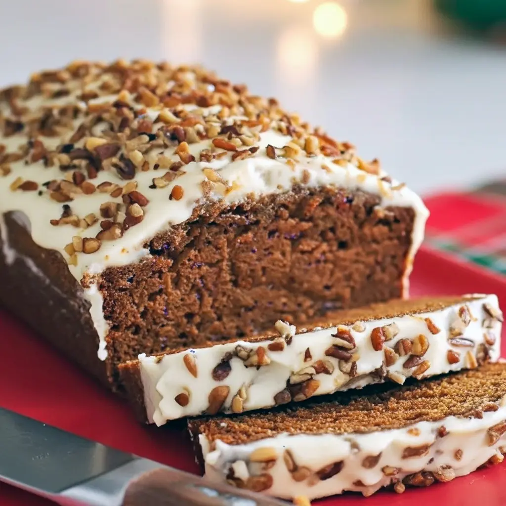 Slice of gingerbread loaf with cream-cheese frosting and chopped pecans on a wooden board — warm, spiced holiday bread.