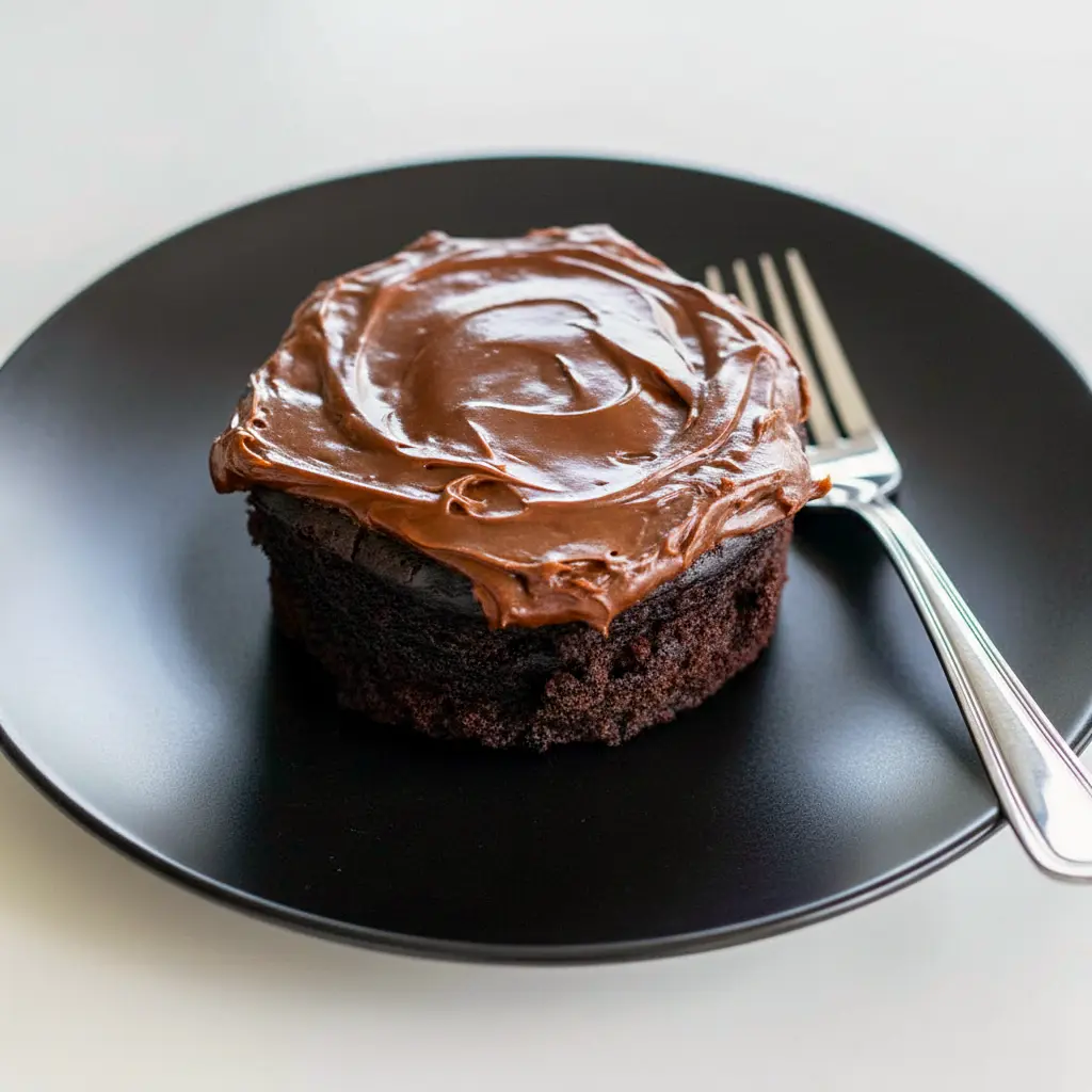 Fudgy chocolate mug cake in a white mug, spoon scooping a warm, gooey center (topped with a small dollop of whipped cream), Quick Chocolate Mug Cake.