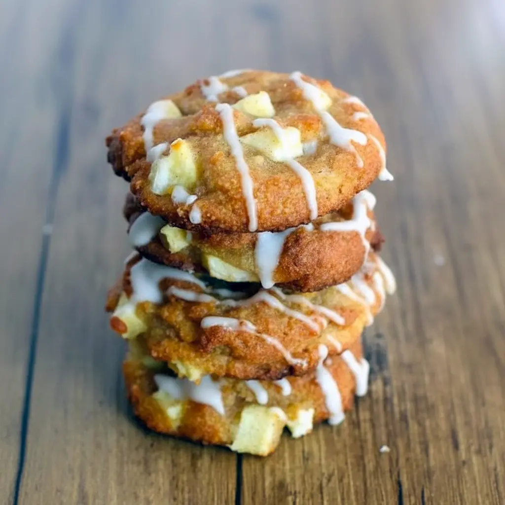Close-up of a glazed keto apple fritter cookies sprinkled with cinnamon sugar and tiny apple pieces on a cooling rack.