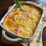 Magic Lemon Cobbler — close-up of a golden square of lemon cobbler with glossy lemon filling, a dusting of powdered sugar, and a melting scoop of vanilla ice cream on the side.