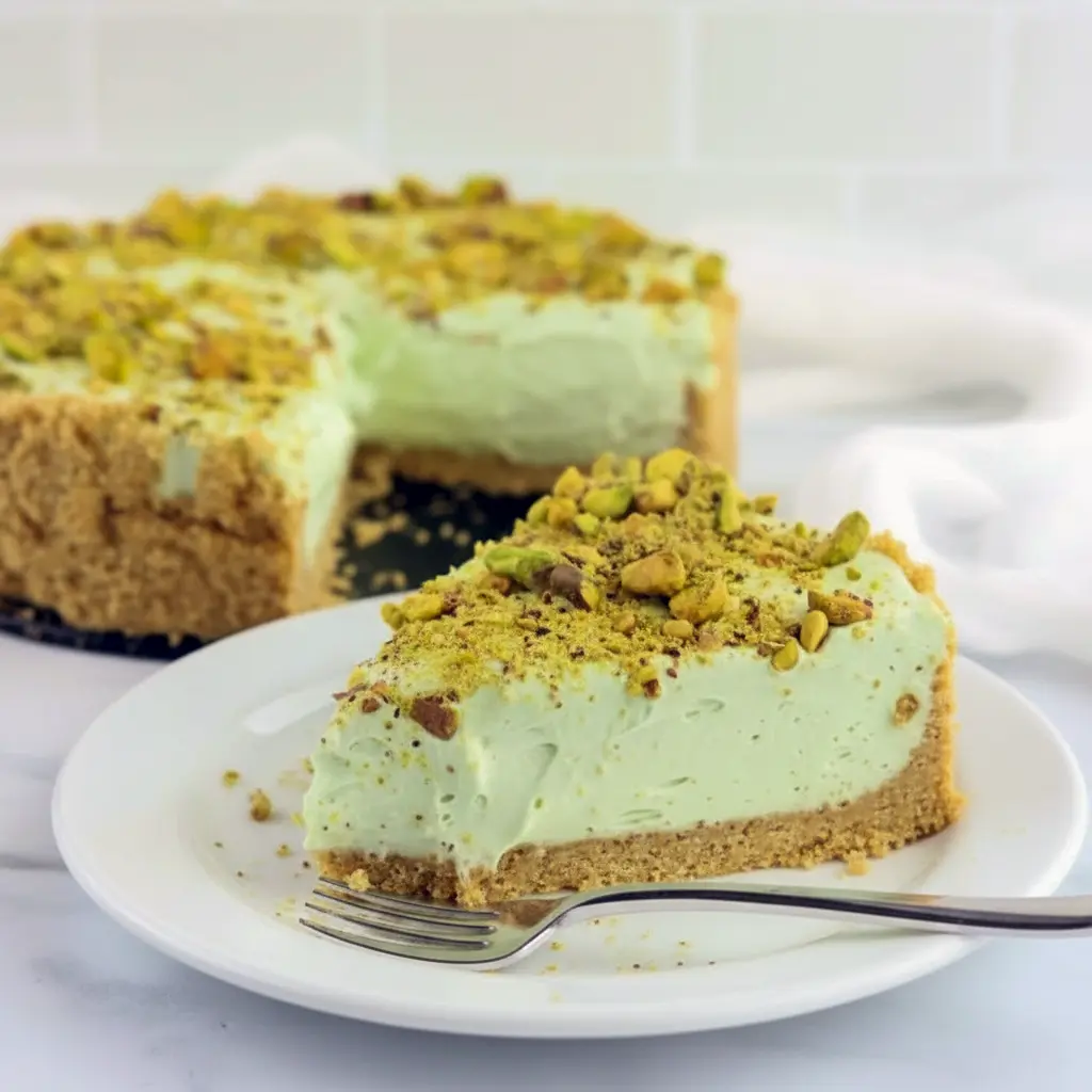Slice of creamy Pistachio Cheesecake with whipped topping and crushed pistachios on a plate — the perfect Easy Pistachio Dessert for pistachio lovers.