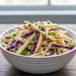 A vibrant bowl of crunchy fall slaw made from cabbage and apples, featuring a creamy tangy dressing for an Apple Coleslaw Recipe, styled to highlight the fresh texture of the Apple Coleslaw Dressing, ideal for an Apple Coleslaw Recipe Easy meal, showcasing the richness of an Apple Coleslaw Recipe With Mayo, perfect as a colorful Fall Apple Coleslaw or crowd-pleasing Potluck Coleslaw, photographed with the same brightness you’d expect from a Cherry Coleslaw Recipe, with crisp slices reminiscent of a Sliced Apple Salad, all tied together with the zing of an Apple Slaw Recipe Cider Vinegar finish.