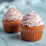 Close-up of a frosted cupcake on a cake stand — Pink Champagne Cupcakes with pearl sprinkles, silky buttercream, and a soft blush hue.