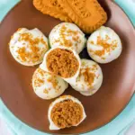 White-chocolate coated Biscoff truffles on a brown plate, one cut in half to show the spiced cookie center, Christmas Baking Recipes.