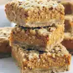 Pumpkin Pie Crumble Bars sliced on parchment, revealing a creamy pumpkin cheesecake center beneath a golden oat-and-pecan streusel topping.