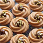 Close-up of coffee butter cookies piped into rosettes, drizzled with dark chocolate and topped with chopped pistachios on a festive plate, Christmas Desserts.