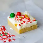 Close-up of frosted Christmas Cookie Bars on a platter, dotted with red and green sprinkles.