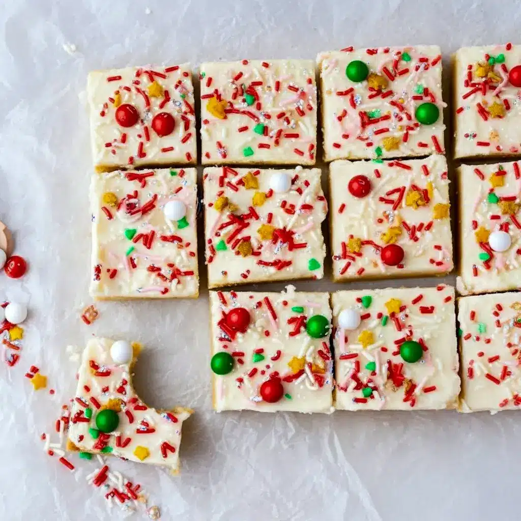 Close-up of frosted Christmas Cookie Bars on a platter, dotted with red and green sprinkles.