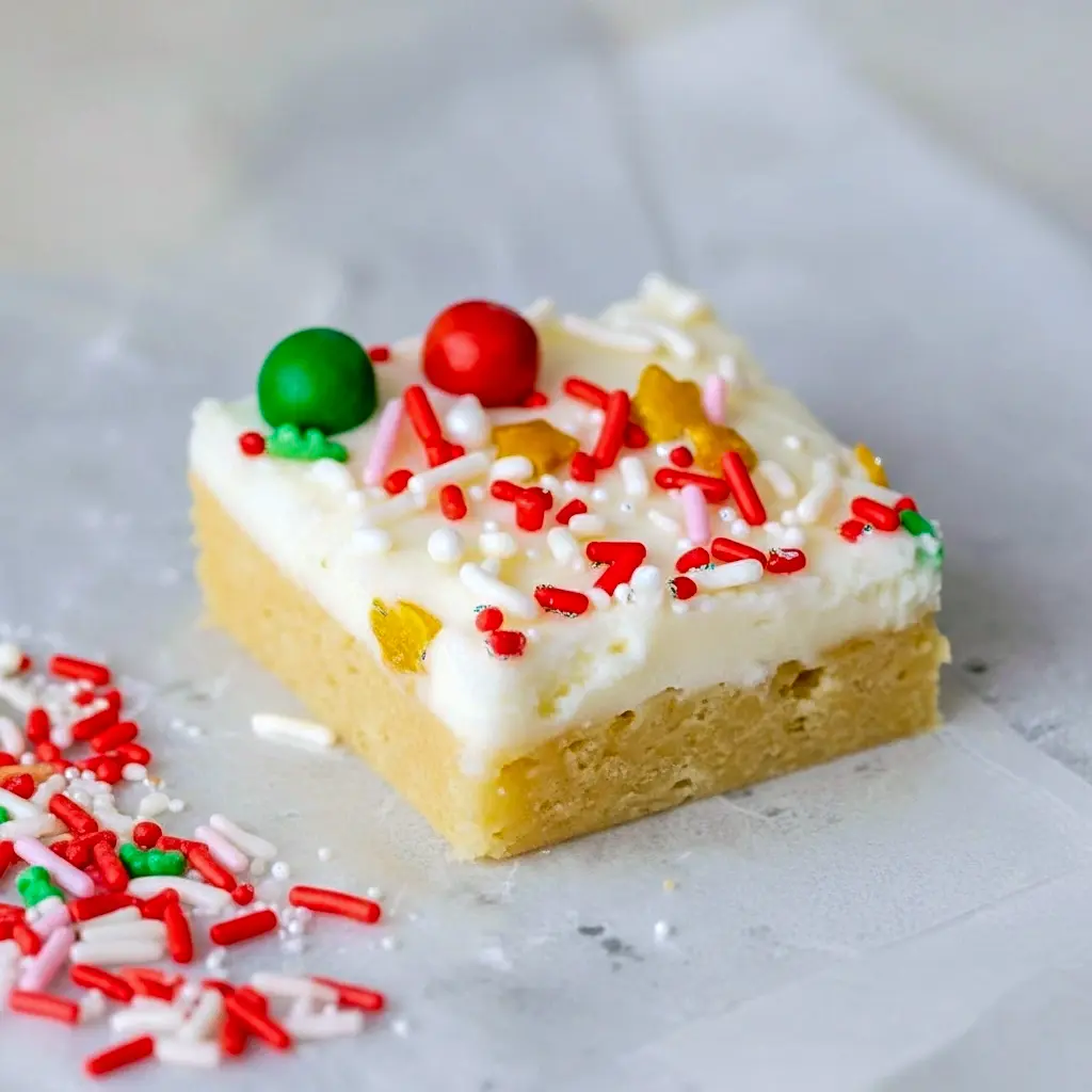 Close-up of frosted Christmas Cookie Bars on a platter, dotted with red and green sprinkles.