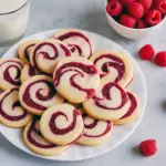 Close-up of golden shortbread rounds with raspberry swirls, some finished with a thin chocolate drizzle, arranged on a festive holiday plate, Christmas Cookies.