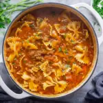 Hearty bowl of lasagna-style soup with bowtie pasta, browned beef, melted mozzarella, dollops of ricotta, grated Parmesan and chopped parsley, served with crusty bread, The Best Lasagna Soup.