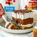 No-bake keto layered dessert with pecan crust, creamy sugar-free cream-cheese layer, chocolate pudding layer and whipped topping, sliced on a serving plate.