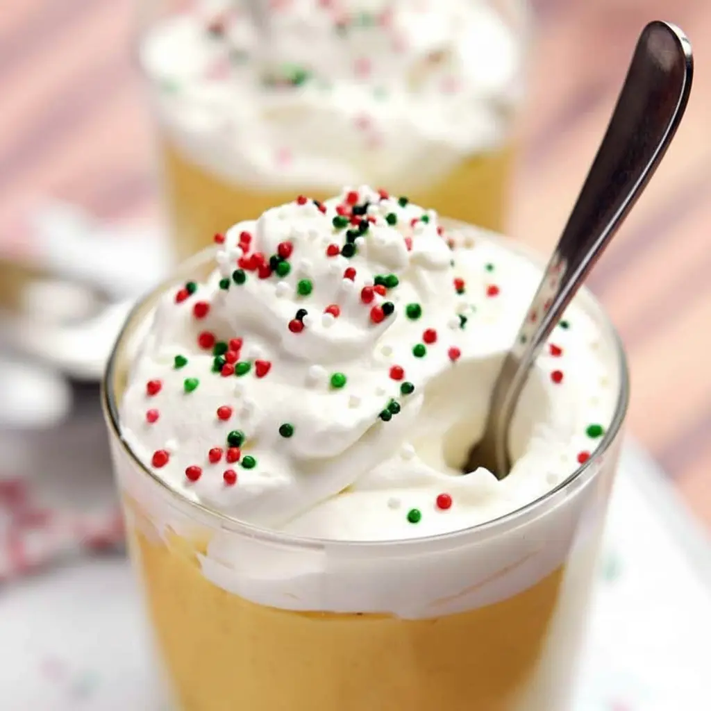 Close-up of a creamy dessert in a glass, crowned with whipped cream and a dusting of nutmeg — festive Slow Cooker Desserts inspired styling and classic Homemade Pudding texture, Eggnog Pudding Recipe.