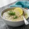 Steaming bowl of Healing Soup (Avgolemono) with shredded chicken, rice, lemon wedge, and a sprinkle of fresh dill — a cozy Avgolemono Soup presentation.