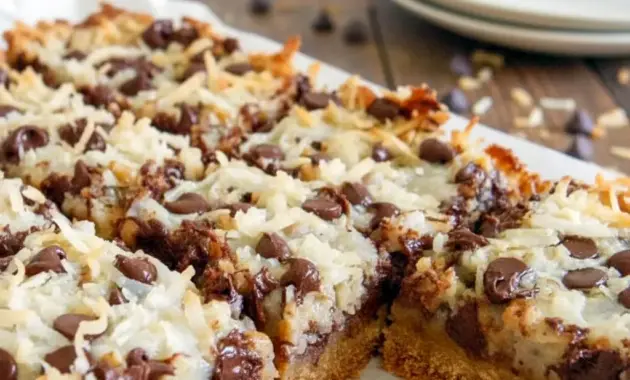 Magic Cookie Bars stacked on a plate, showing gooey chocolate chips, toasted coconut, and chopped nuts.