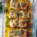 Close-up of flaky, golden-baked cod drizzled with lemon-garlic oil and sprinkled with parsley — a tasty example of Mediterranean Cooking and a top choice among Mediterranean Cod Recipes.