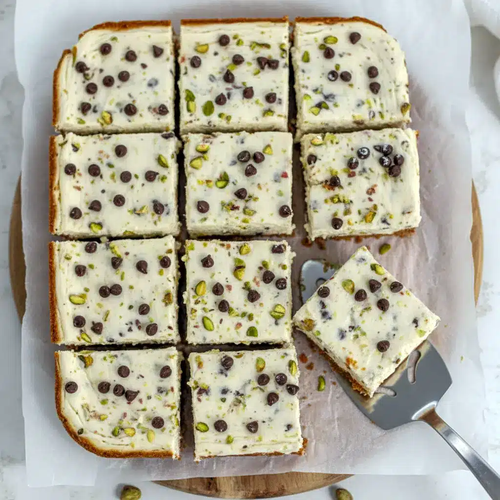 Square no-bake cannoli cheesecake bars on a serving plate, topped with mini chocolate chips and chopped pistachios.