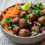 Close-up of glossy Banh Mi Meatballs topped with shredded carrot, cilantro, and sliced jalapeño; a plated example of Vietnamese Meatballs Recipe and savory Vietnamese Meatballs ready to serve.