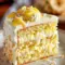 Coconut Pineapple Dream Cake Recipe — slice of golden cake topped with shredded toasted coconut, pineapple chunks, and creamy coconut frosting on a white plate.