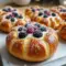Vanilla Cheesecake Danish carnival bun with blueberry compote and a dusting of powdered sugar on a white plate.
