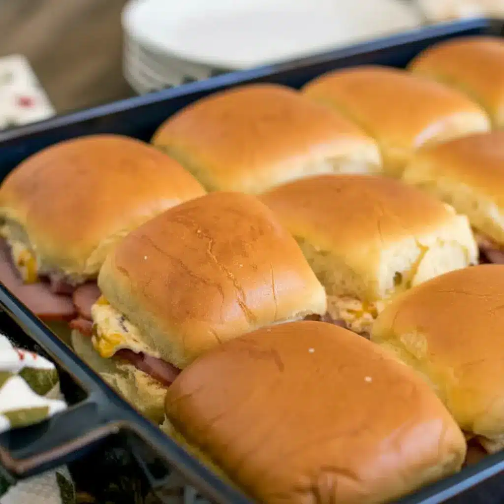 Golden, butter-brushed ham sliders on a wooden board, a perfect example of Sandwiches With Hawaiian Rolls, Sandwiches On Hawaiian Rolls, and easy Sandwich Recipes With Hawaiian Rolls, also adaptable for Sliders Cold Sandwich Recipes and served as a classic Sandwich On Hawaiian Rolls, Sandwiches Using Hawaiian Rolls.