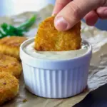 Golden quinoa-coated chicken nuggets stacked on a plate with a small bowl of dipping sauce and carrot sticks on the side, Quinoa Chicken Nuggets.
