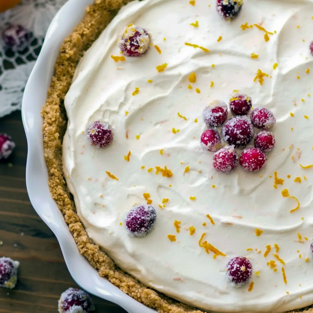 Slice of no-bake cranberry orange cream pie on a plate, graham cracker crust, orange whipped cream, and sugared cranberries on top, Holiday Cream Pie.