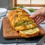 Golden pull-apart loaf layered with melted cheese, garlic butter, and parsley on a wooden board with a small bowl of marinara dip, Pull Apart Garlic Bread.