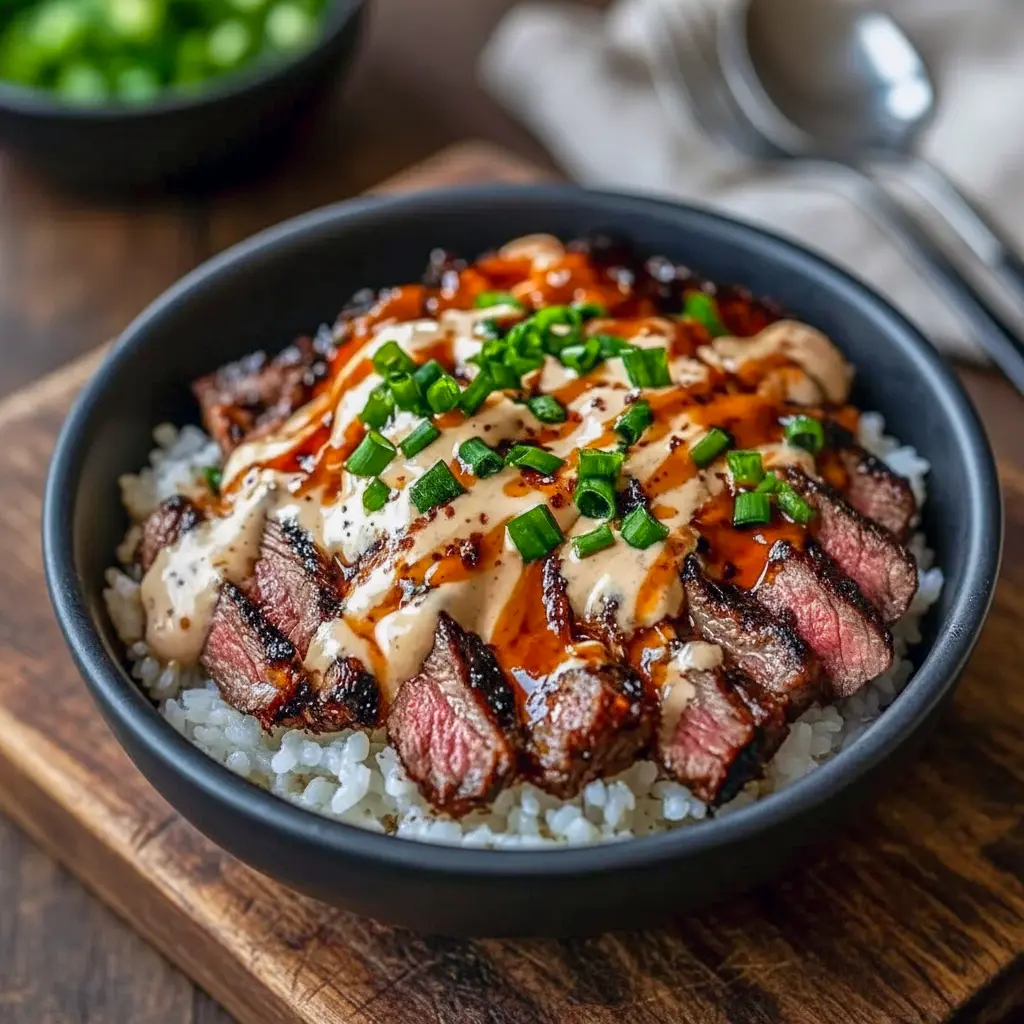 Close-up of a bowl with thinly sliced marinated steak over steamed rice, sautéed bell peppers and broccoli, drizzled with a spicy cream sauce and finished with sesame seeds and chopped green onions, Korean Bbq.