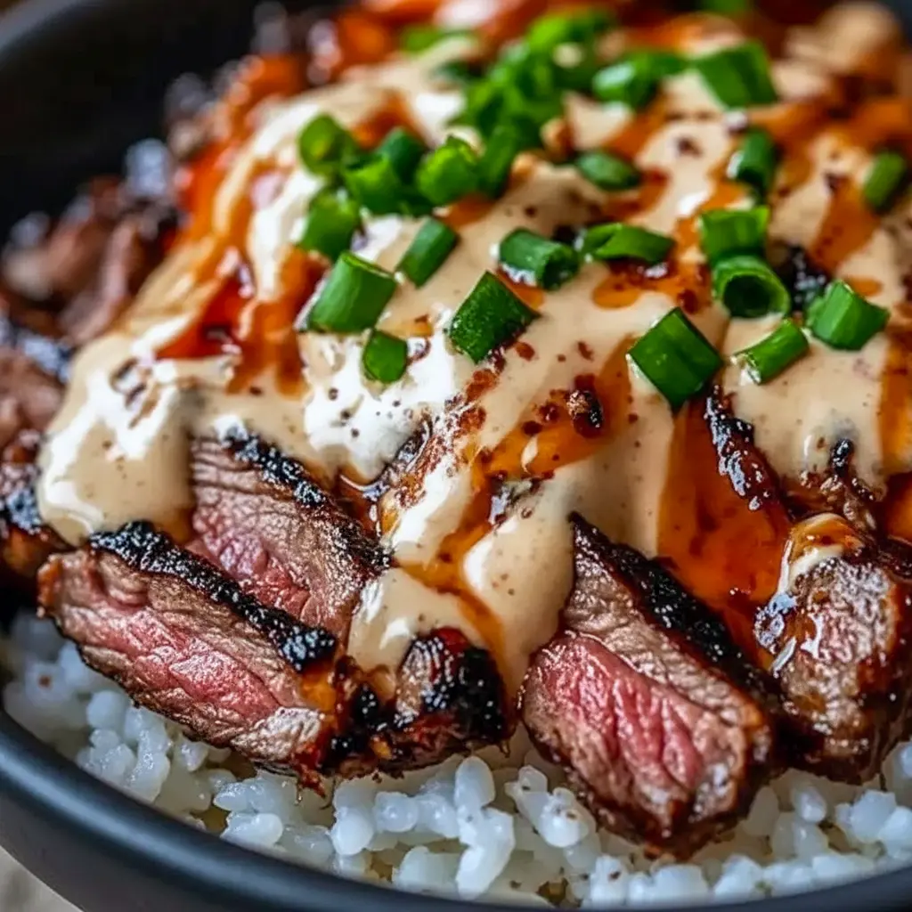 Close-up of a bowl with thinly sliced marinated steak over steamed rice, sautéed bell peppers and broccoli, drizzled with a spicy cream sauce and finished with sesame seeds and chopped green onions, Korean Bbq.