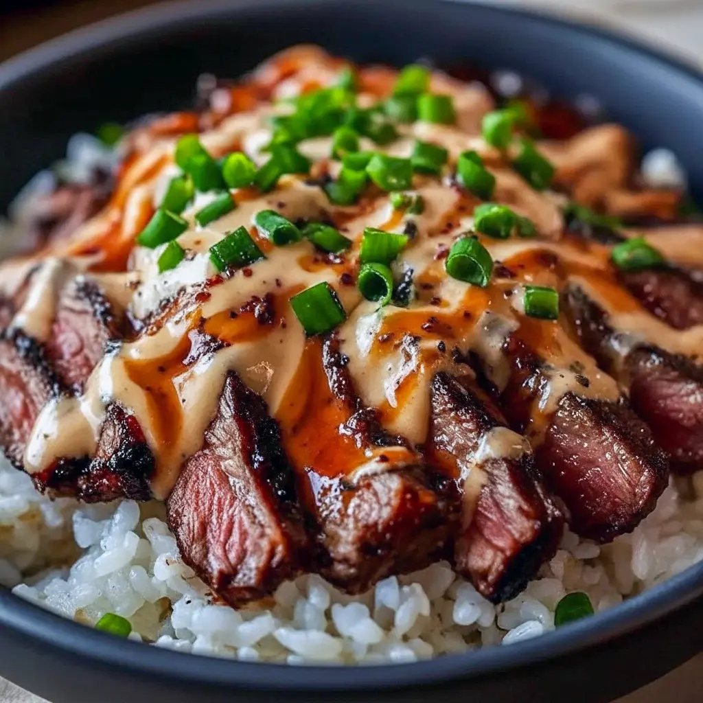 Close-up of a bowl with thinly sliced marinated steak over steamed rice, sautéed bell peppers and broccoli, drizzled with a spicy cream sauce and finished with sesame seeds and chopped green onions, Korean Bbq.