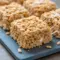 Close-up of two stacked Churro Rice Krispie bars, golden with cinnamon-sugar coating and gooey marshmallow pulls.