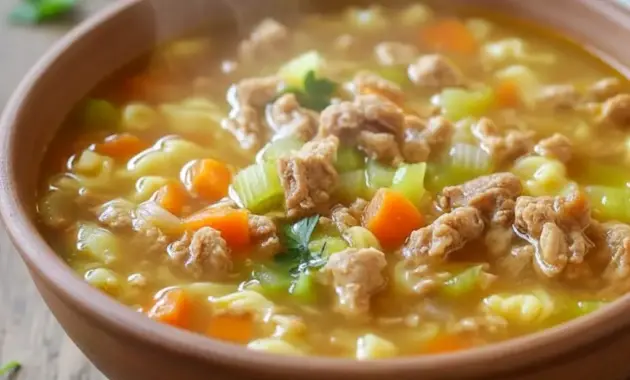Close-up bowl of Homemade Soup Recipe egg roll soup showing pork, shredded cabbage, carrot ribbons, sliced green onions, and a halved boiled egg.