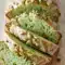 Slice of Pistachio Pudding Bread with pale green crumb and crushed pistachio topping, presented on a wooden board — a soft Pistachio Bread ideal for brunch or dessert.