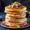 Stack of Savory Pancakes topped with crispy bacon, chorizo bits, melted cheddar, a dollop of chili butter and a glossy golden-syrup drizzle.