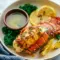 Broiled Lobster Tail Recipe topped with garlic-herb butter, lemon wedge, and chopped parsley on a serving plate.